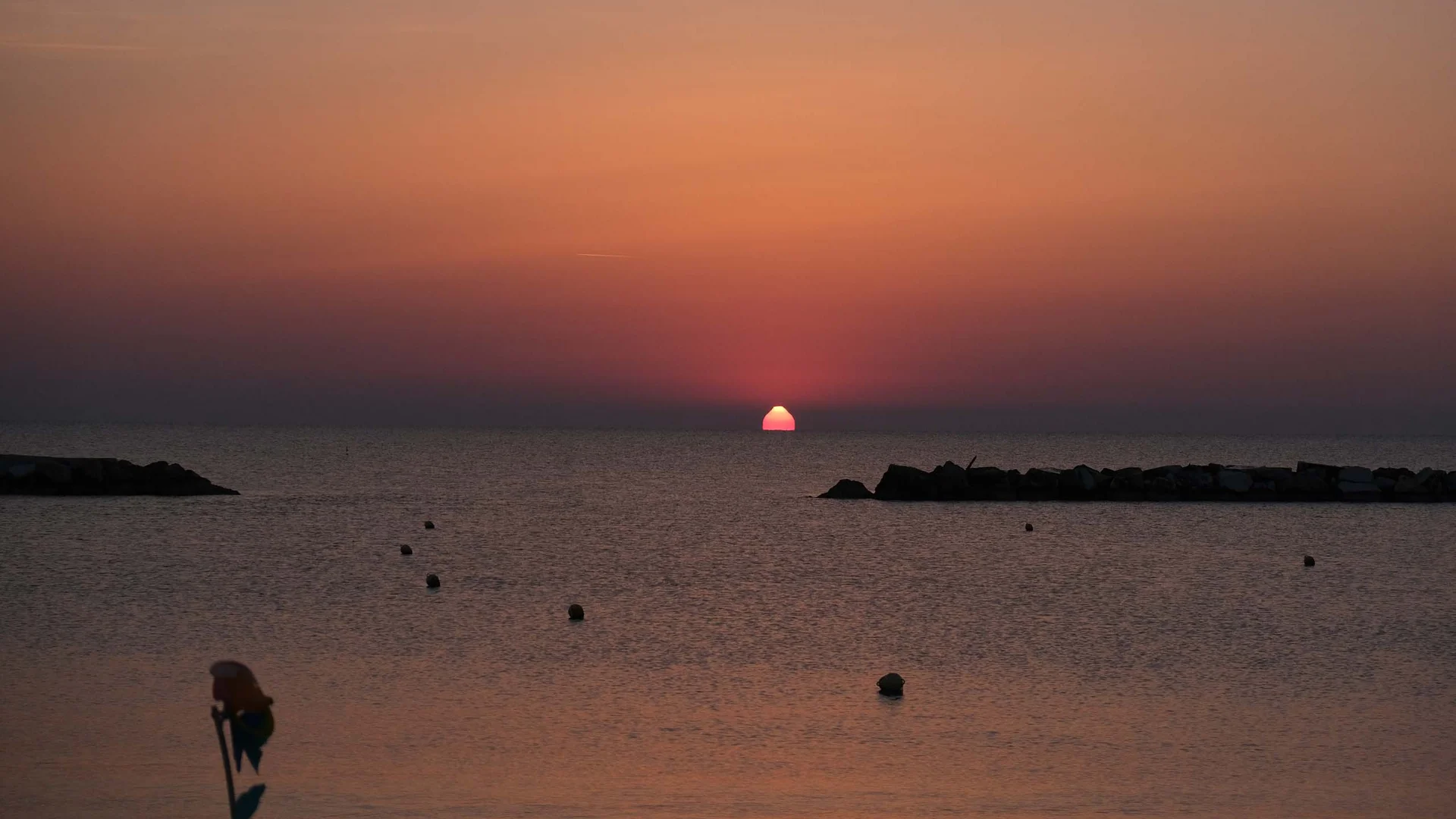 Tramonto sul mare con sole che sfiora l'orizzonte e cielo arancione