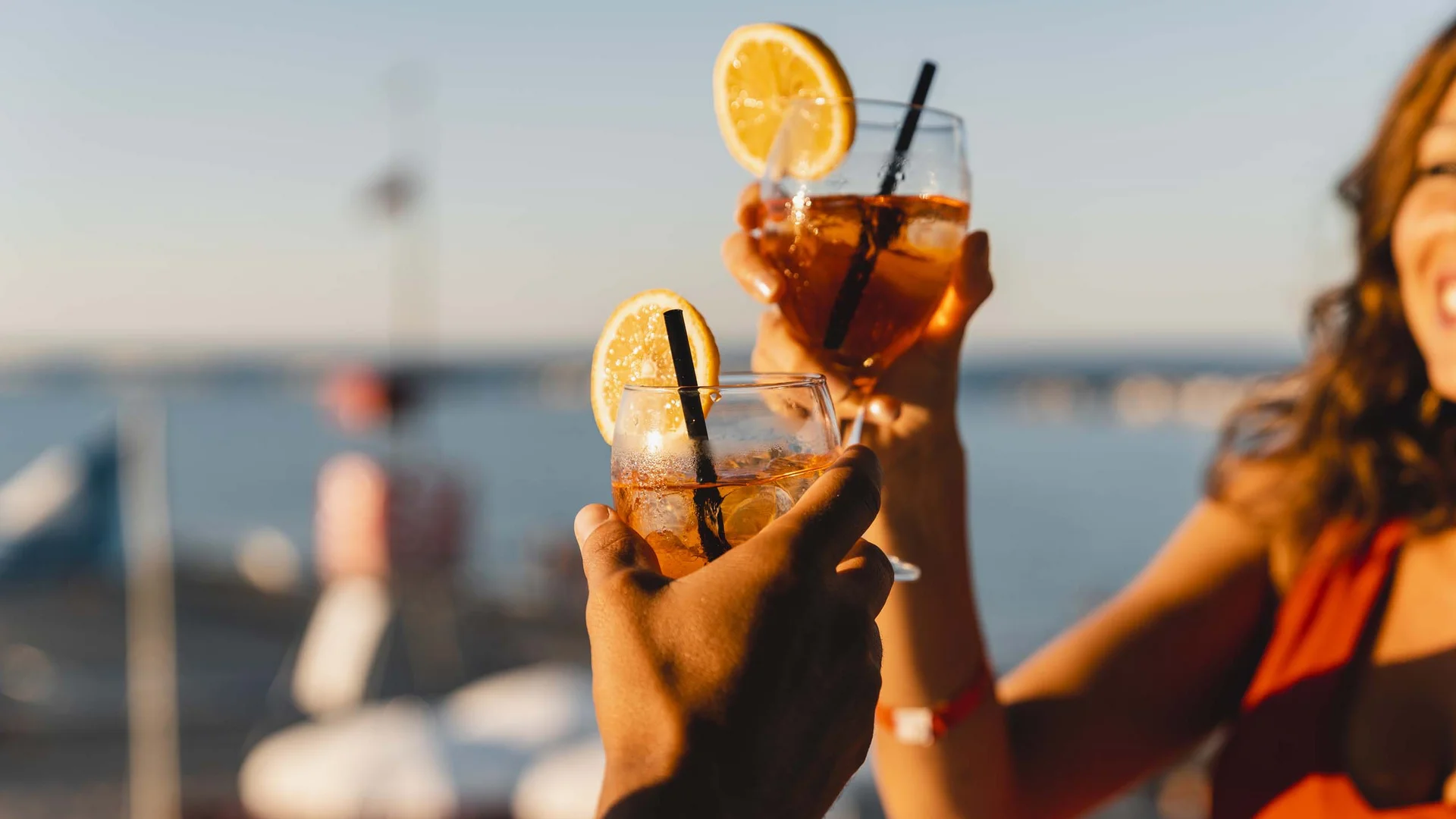 Personen stoßen mit Cocktails und Zitronenscheiben vor Meereskulisse an