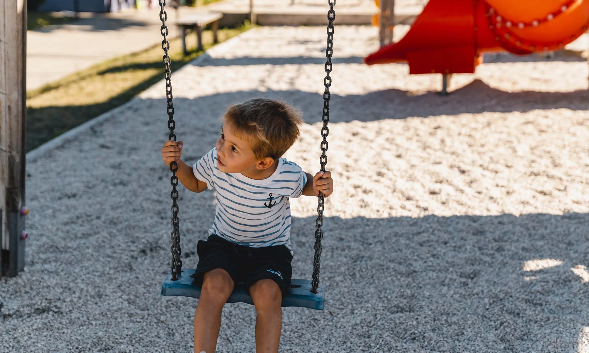 Kind sitzt auf Schaukel auf einem Spielplatz im Freien