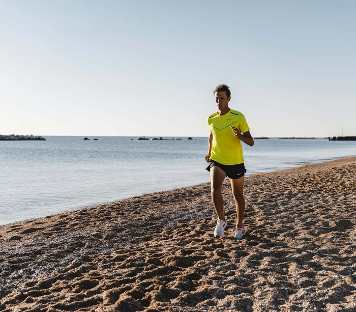 Mann läuft morgens am Strand mit gelbem T-Shirt
