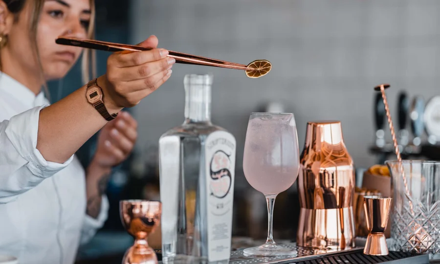 Bartender che decora cocktail con fetta di limone essiccato usando pinze
