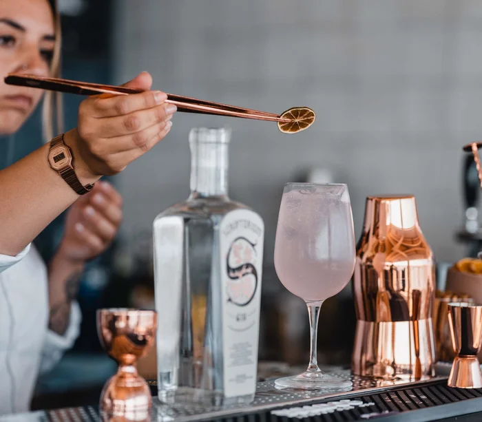 Bartender che decora cocktail con fetta di limone essiccato usando pinze