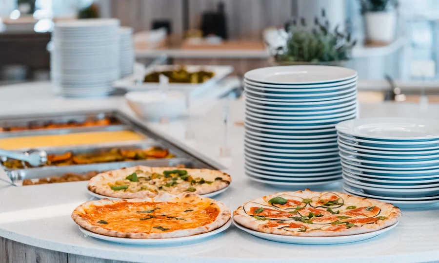 Drei Pizzen auf weißen Tellern neben einem Stapel leerer Teller auf einer Theke