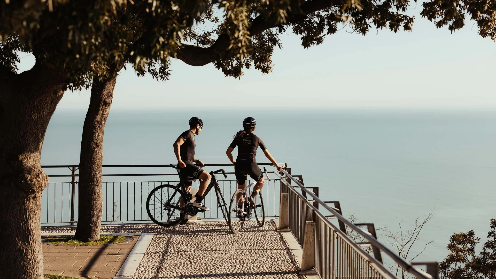 Due ciclisti in abbigliamento sportivo guardano il mare da un belvedere