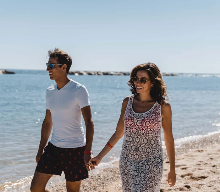 Coppia sorridente che cammina mano nella mano sulla spiaggia al sole