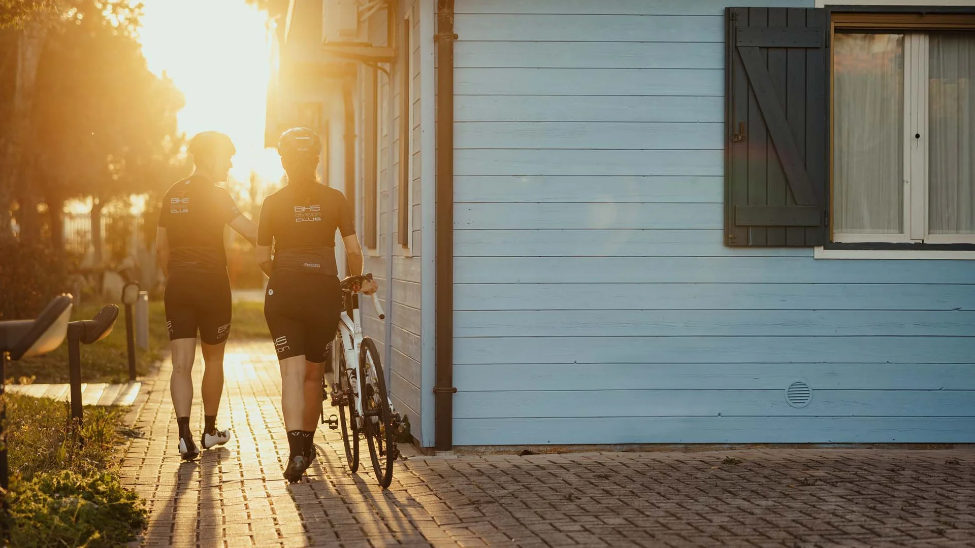 Zwei Radfahrer gehen bei Sonnenuntergang an einem blauen Haus vorbei