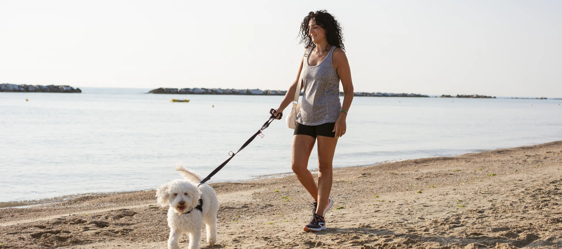 Un resort pet-friendly nelle Marche | Natural Village Resort Donna passeggia con un cane bianco al guinzaglio su una spiaggia