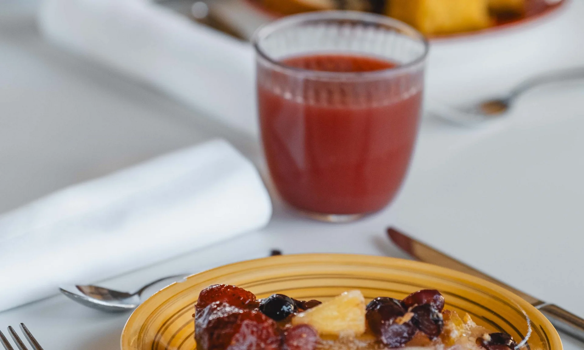 Stück Obstkuchen auf gelbem Teller mit Glas rotem Saft