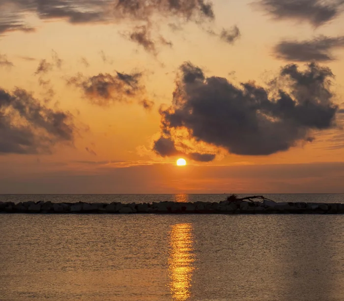 Tramonto sul mare con nuvole scure e riflesso dorato sull'acqua
