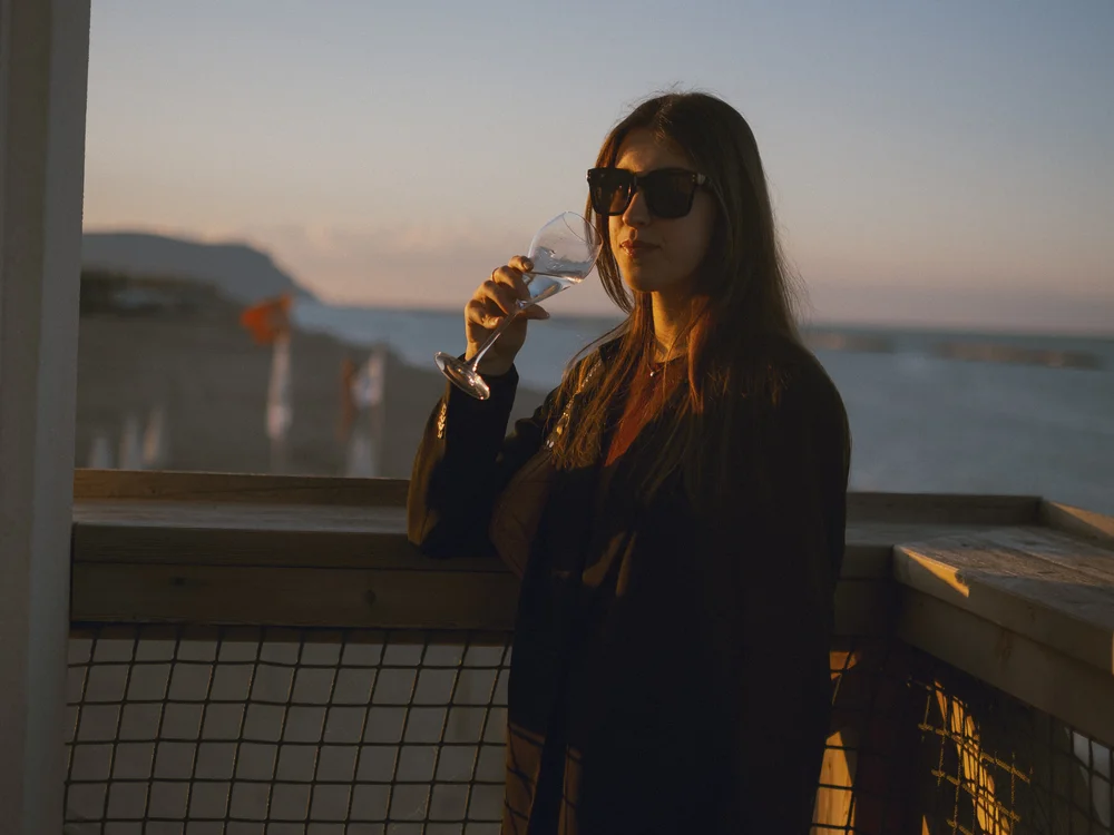 Donna con occhiali da sole che beve da un bicchiere sulla terrazza al tramonto