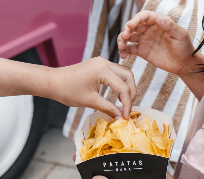 Mani di bambini che prendono patatine da un contenitore nero con scritta