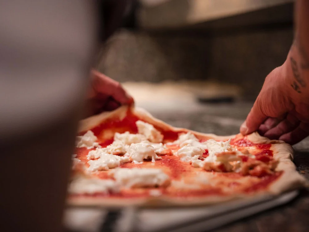 Hände bereiten Pizza mit Tomatensoße und Mozzarella auf rohem Teig zu