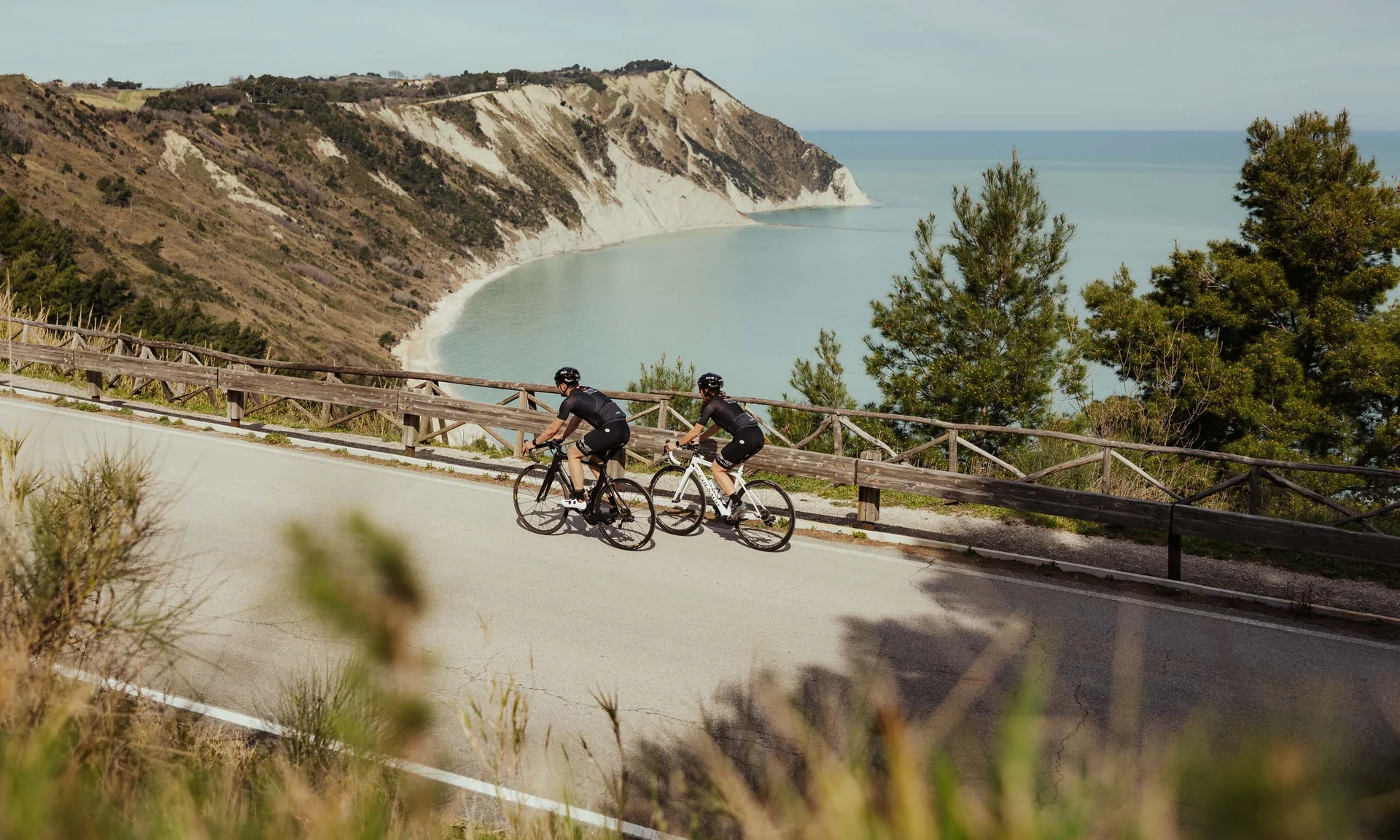 Zwei Radfahrer in Sportkleidung auf Straße mit Klippe und Meer im Hintergrund