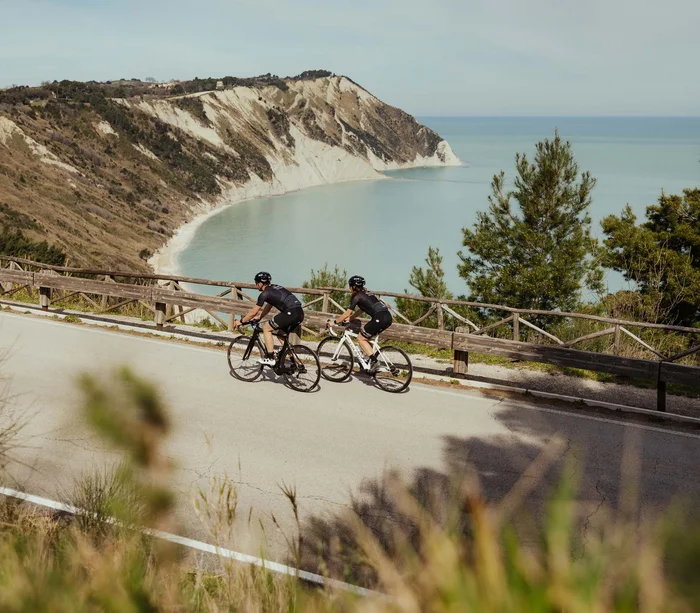 Zwei Radfahrer in Sportkleidung auf Straße mit Klippe und Meer im Hintergrund