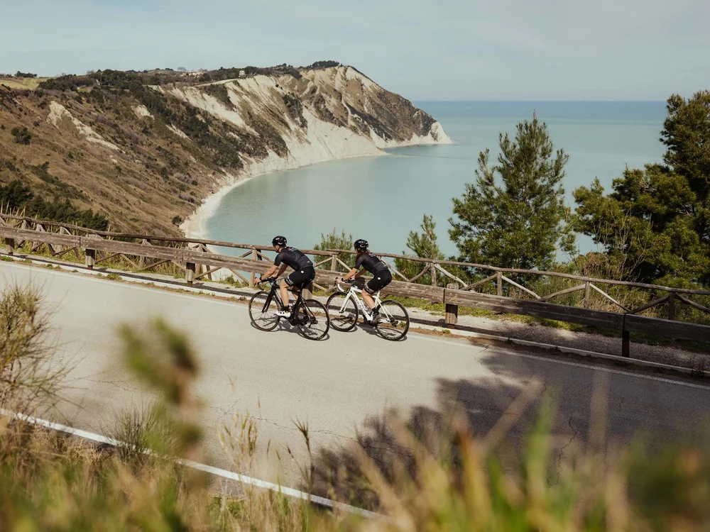 Zwei Radfahrer in Sportkleidung auf Straße mit Klippe und Meer im Hintergrund