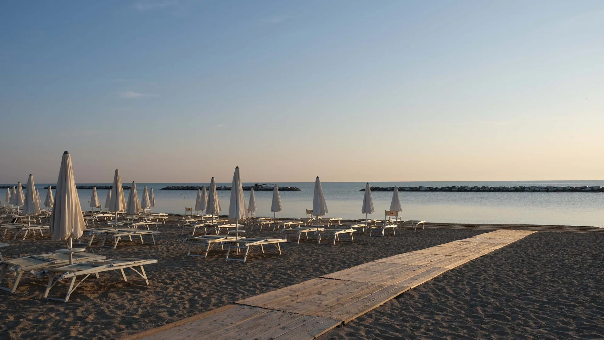 Spiaggia deserta con ombrelloni chiusi e sdraio all'alba o al tramonto