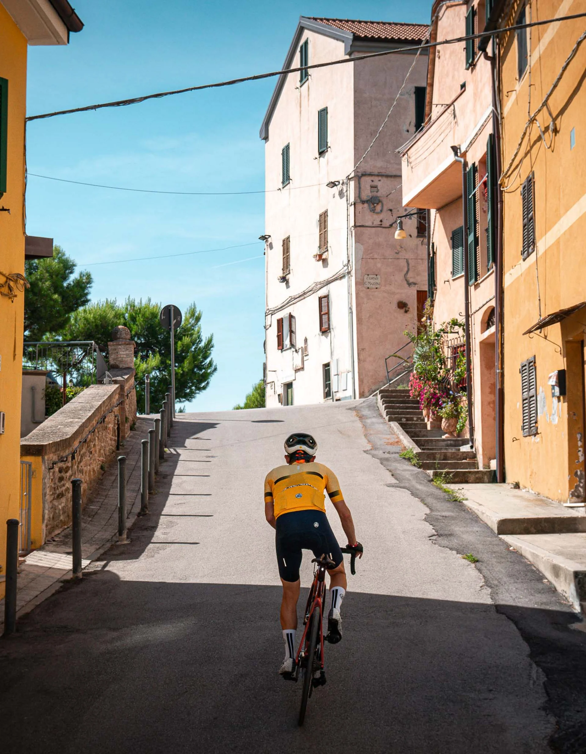Radfahrer in gelbem Trikot fährt einen Hügel in einem Dorf mit bunten Häusern hinauf