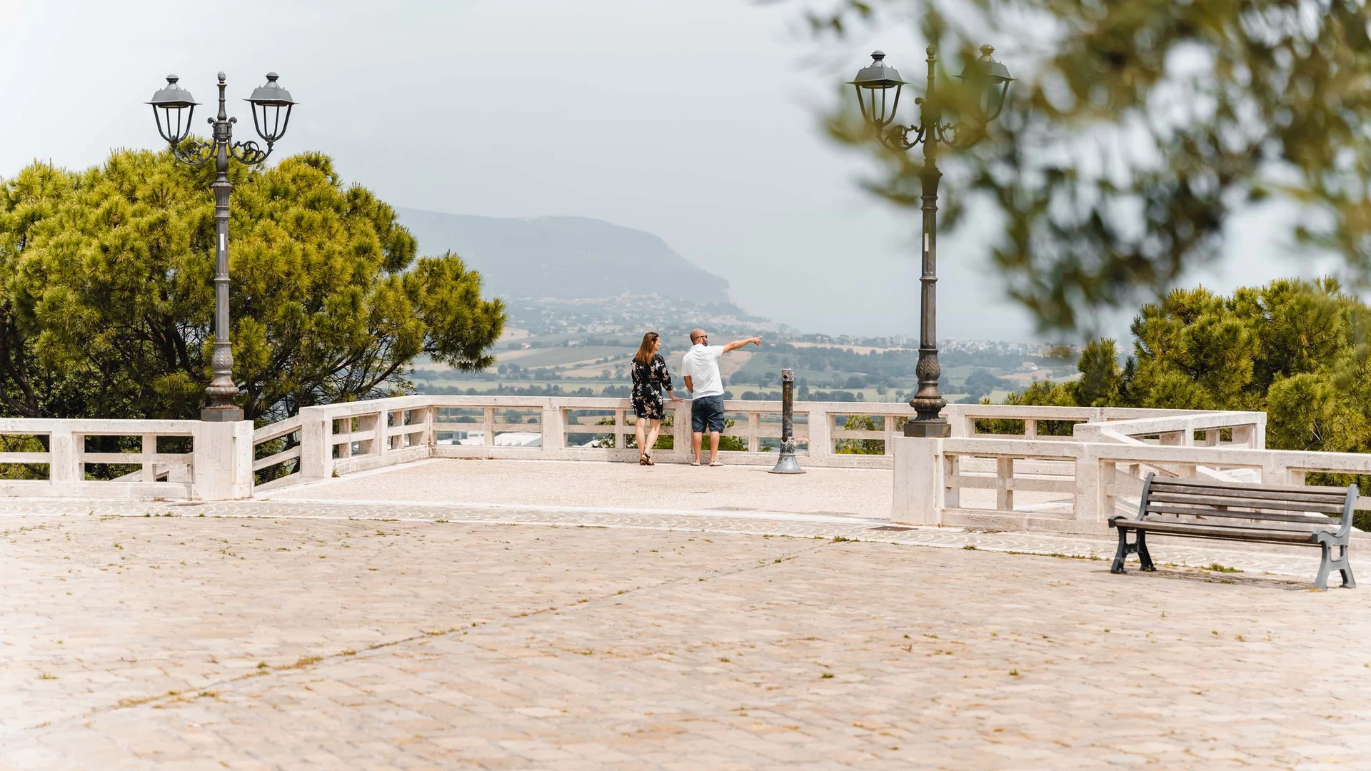 Coppia che osserva il paesaggio da una terrazza con lampioni e panchina