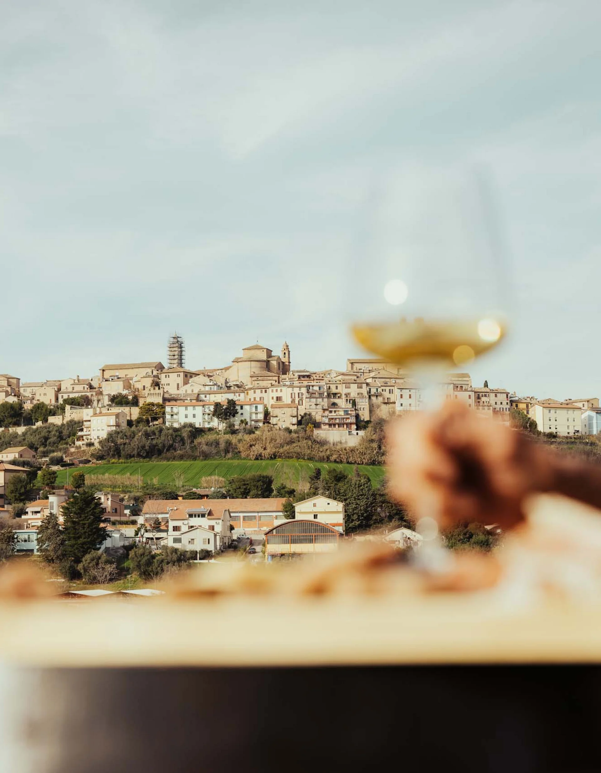 Blick auf eine Hügelstadt mit einer Hand, die ein Glas Weißwein hält