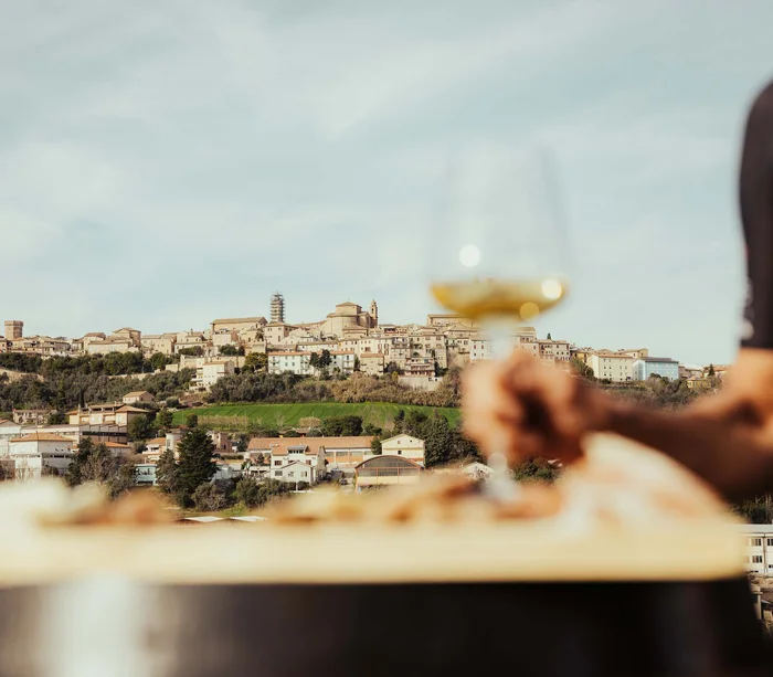 Blick auf eine Hügelstadt mit einer Hand, die ein Glas Weißwein hält