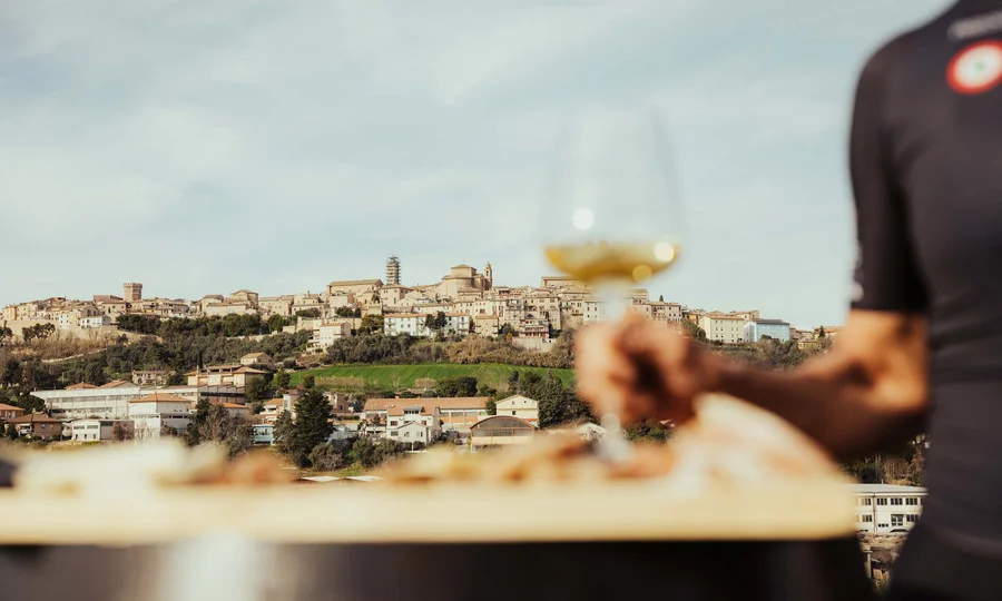 Blick auf eine Hügelstadt mit einer Hand, die ein Glas Weißwein hält