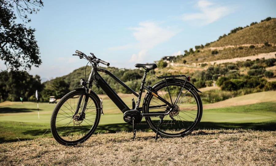 Schwarzes E-Bike auf Wiese mit Hügeln im Hintergrund.
