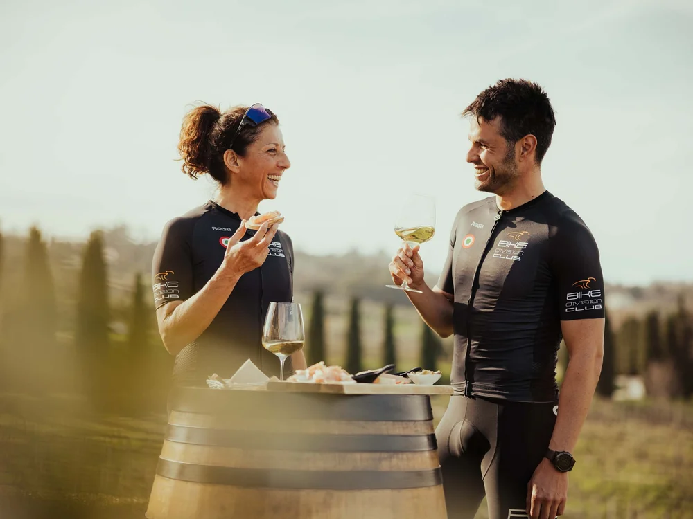 Zwei Radfahrer genießen Wein und Snacks draußen mit hügeliger Landschaft