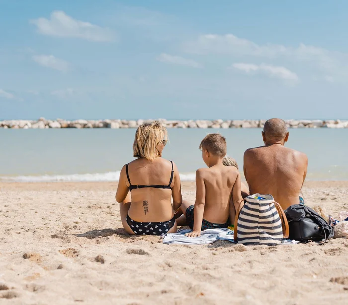 Famiglia seduta sulla spiaggia con vista sul mare e scogliere distanti