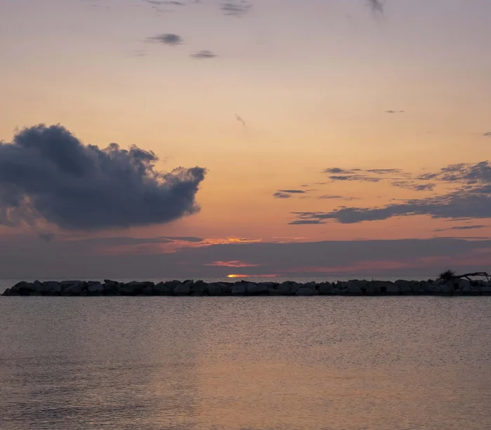 Tramonto sul mare con cielo nuvoloso e rocce all'orizzonte