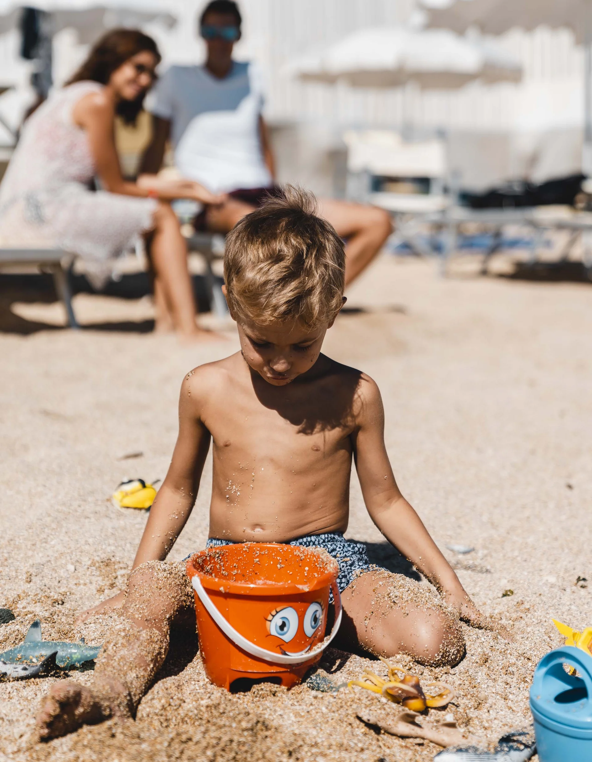 Kind spielt mit orangene Eimer am sandigen Strand