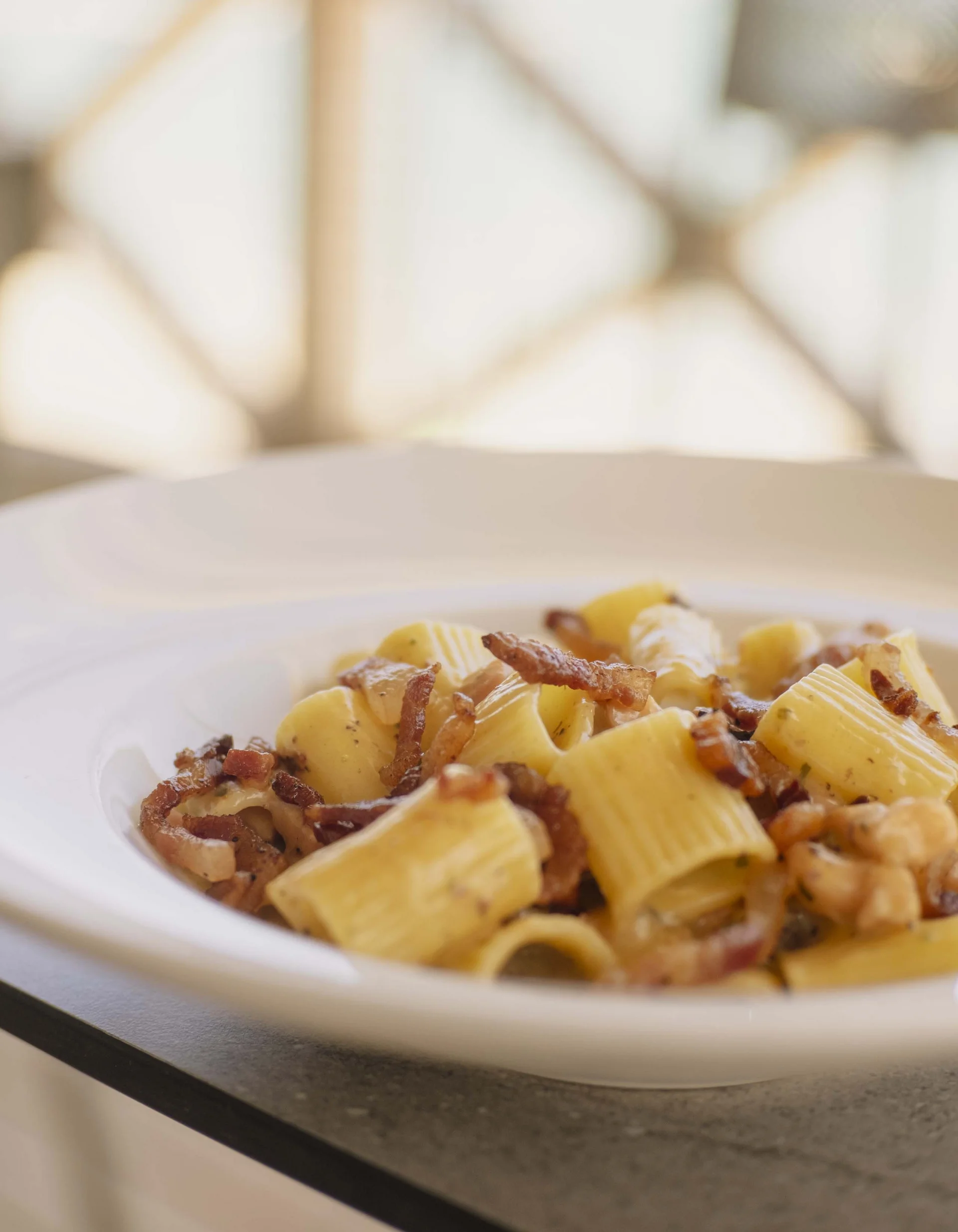 Rigatoni Pasta mit knusprigem Speck auf weißem Teller