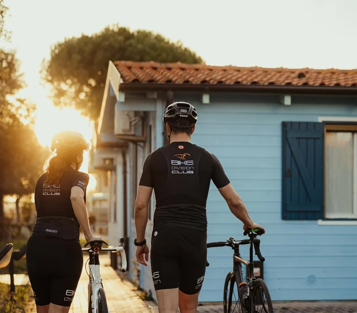 Zwei Radfahrer schieben ihre Fahrräder bei Sonnenuntergang zu einem blauen Haus