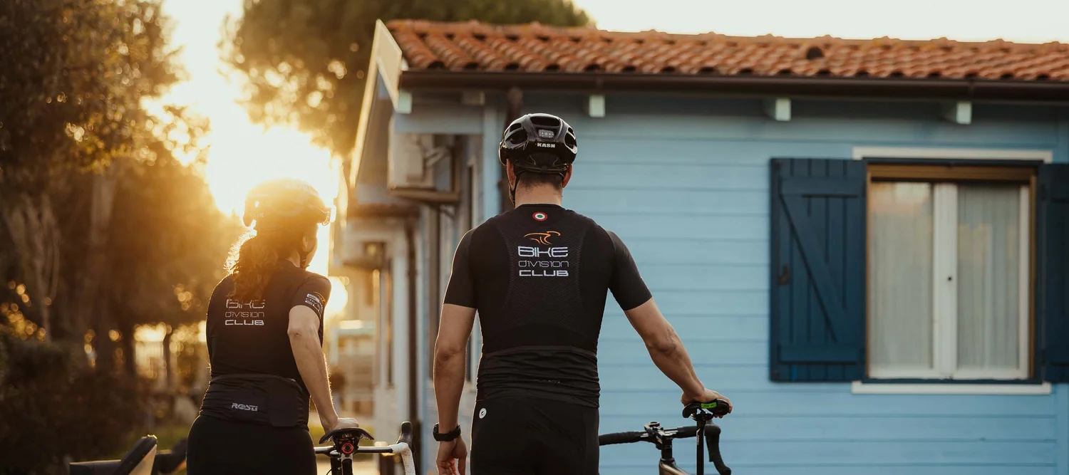 Due ciclisti spingono le biciclette verso una casa blu al tramonto