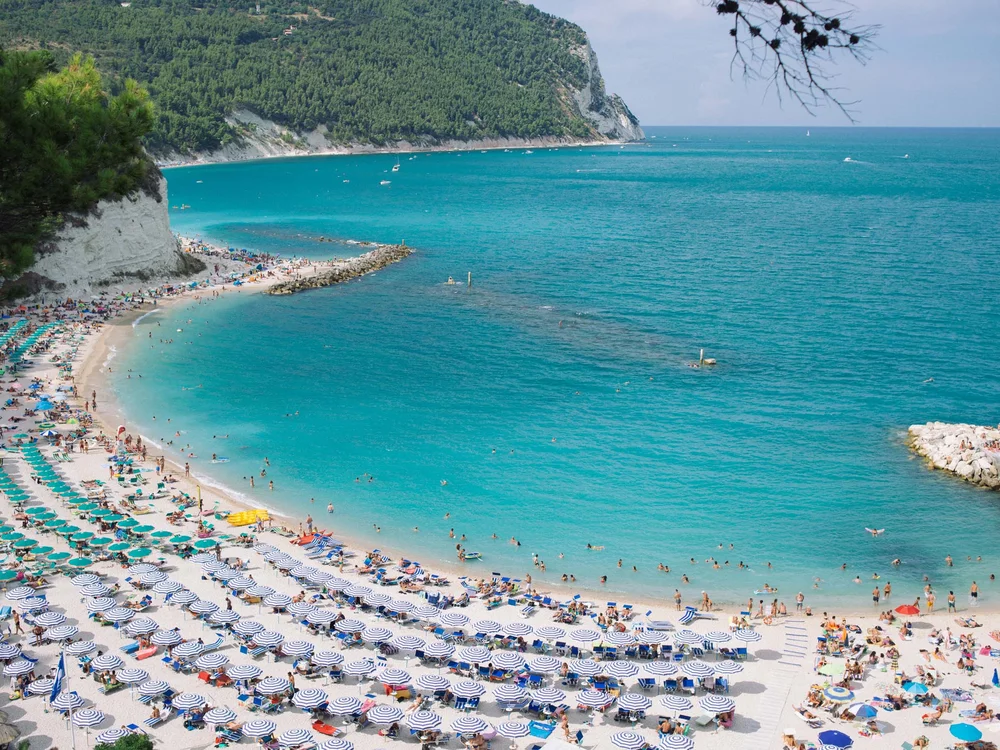 Spiaggia affollata con ombrelloni e mare turchese con scogliere verdi