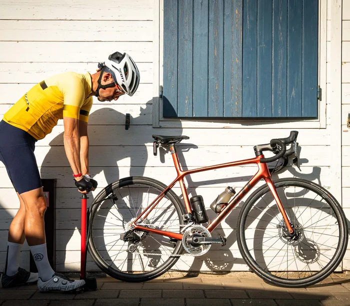 Radfahrer mit Helm pumpt Vorderreifen eines Rennrads auf