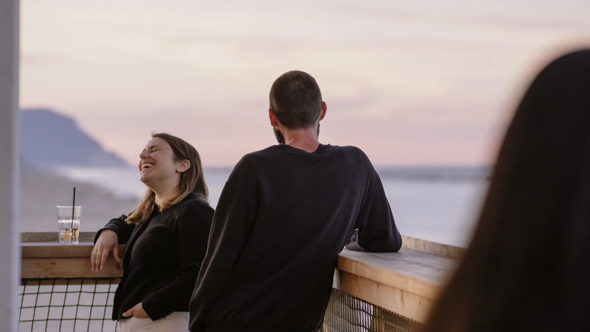 Zwei Personen sprechen und lachen auf einem Balkon bei Sonnenuntergang