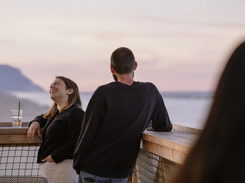 Due persone chiacchierano e ridono su un balcone al tramonto