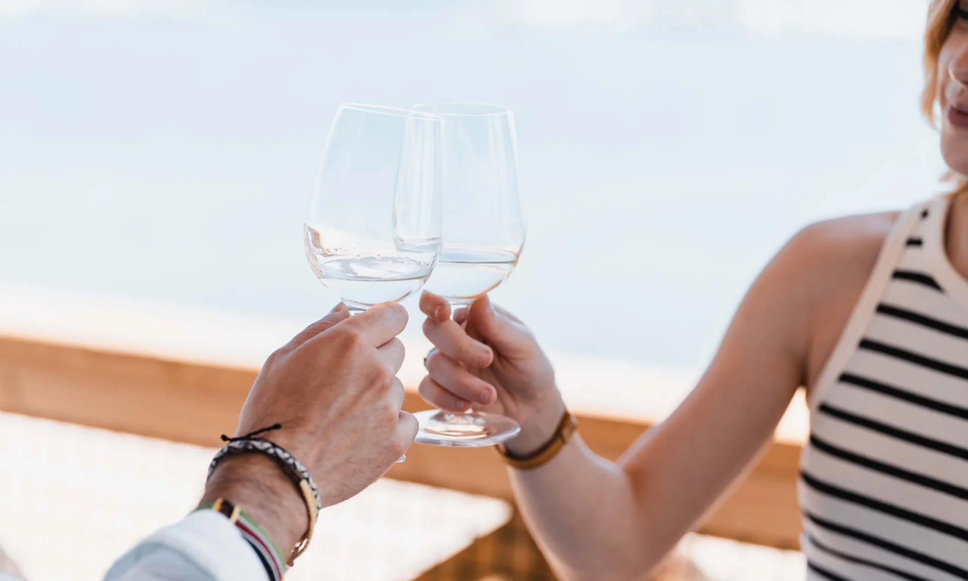 Zwei Personen stoßen mit Gläsern Weißwein im Freien an