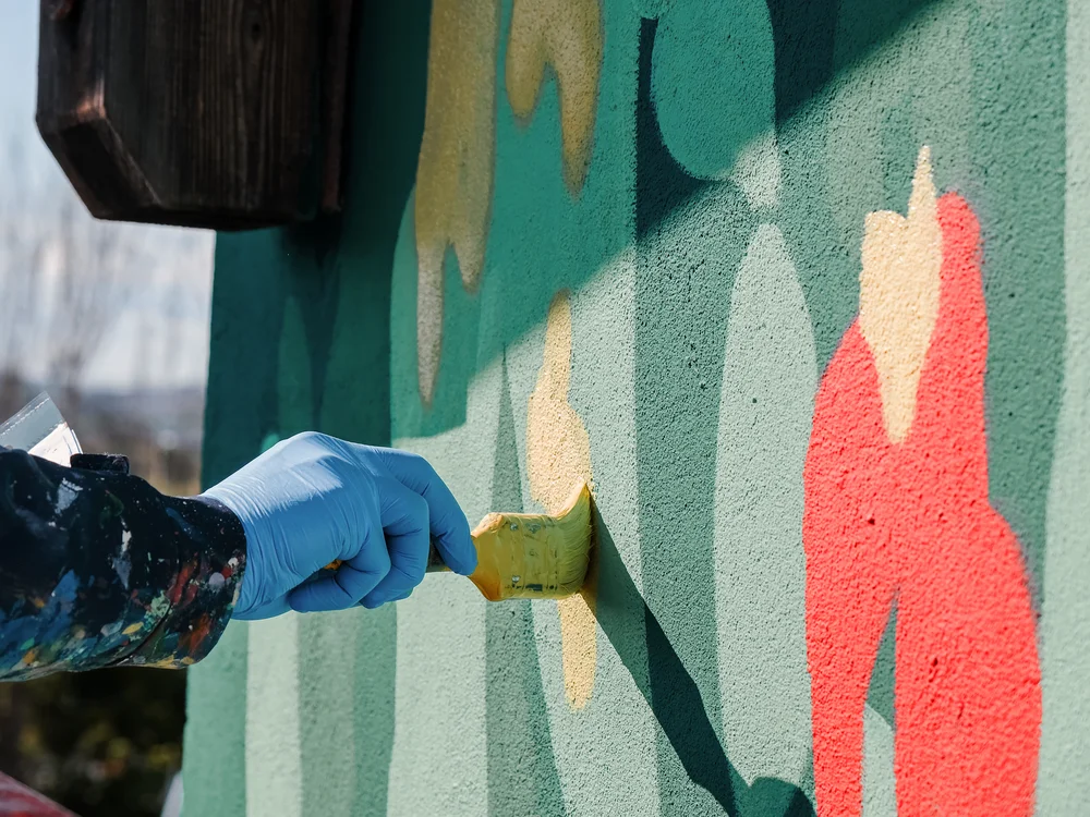 Mano con guanto blu che dipinge un murale colorato con un pennello
