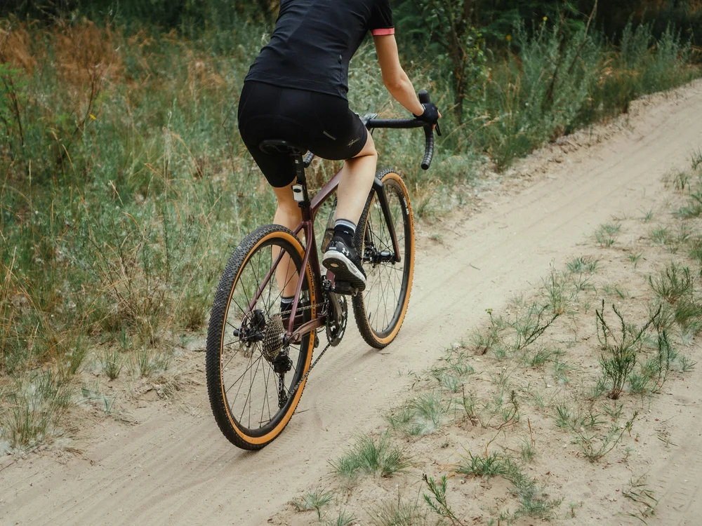 Ciclista con abbigliamento nero su strada di ghiaia in natura