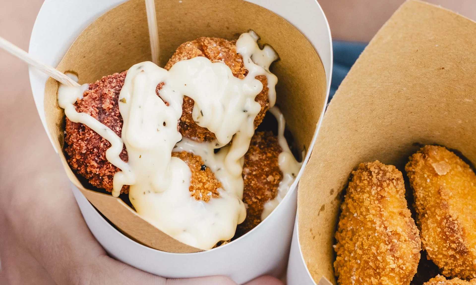 Hände halten Croquettes mit weißer Soße in Pappbechern