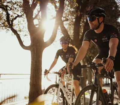 Due ciclisti in abbigliamento da corsa pedalano al sole vicino a un albero